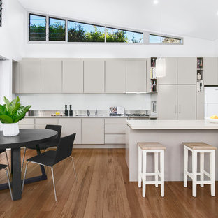 Photo of a mid-sized contemporary galley eat-in kitchen in Sydney with a double-bowl sink, grey cabinets, quartz benchtops, white splashback, glass sheet splashback, stainless steel appliances, medium hardwood floors, with island, white benchtop, flat-panel cabinets and brown floor.
