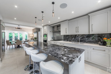 Example of a classic gray floor eat-in kitchen design in Hertfordshire with an integrated sink, flat-panel cabinets, gray cabinets, granite countertops, gray backsplash, stainless steel appliances and an island