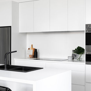 Design ideas for a contemporary galley kitchen in Melbourne with a drop-in sink, flat-panel cabinets, white cabinets, stainless steel appliances, medium hardwood floors, with island, brown floor and white benchtop.