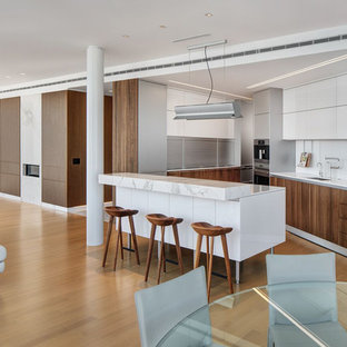 Diseño de cocina en U, contemporánea, abierta, con fregadero bajoencimera, armarios con paneles lisos, puertas de armario de madera en tonos medios, salpicadero blanco, salpicadero de vidrio templado, electrodomésticos de acero inoxidable, suelo de madera en tonos medios y una isla