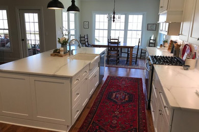 Large transitional galley medium tone wood floor and brown floor eat-in kitchen photo in Other with a farmhouse sink, shaker cabinets, white cabinets, marble countertops, white backsplash, subway tile backsplash, stainless steel appliances, an island and white countertops