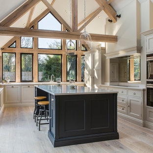 Photo of a traditional u-shaped kitchen in Oxfordshire with beaded cabinets, quartz worktops, light hardwood flooring, an island, grey cabinets, black appliances, beige floors and grey worktops.