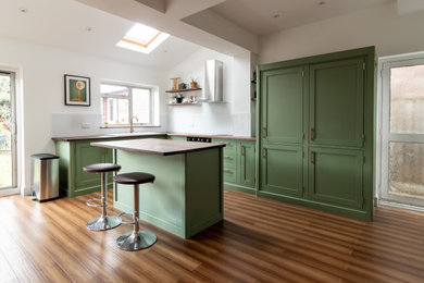 Photo of a medium sized classic l-shaped kitchen/diner in Cheshire with a built-in sink, shaker cabinets, green cabinets, wood worktops, an island, brown worktops, white splashback, integrated appliances, brown floors, metro tiled splashback and dark hardwood flooring.