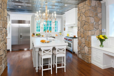 Example of a large classic l-shaped medium tone wood floor and brown floor eat-in kitchen design in Other with a farmhouse sink, beaded inset cabinets, white cabinets, white backsplash, stainless steel appliances, an island, marble countertops and subway tile backsplash