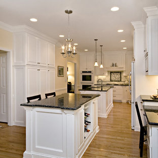 Large traditional eat-in kitchen ideas - Example of a large classic l-shaped eat-in kitchen design in Raleigh with an undermount sink, raised-panel cabinets, white cabinets, granite countertops, white backsplash, subway tile backsplash, white appliances and two islands