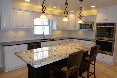 Example of a mid-sized u-shaped ceramic tile open concept kitchen design in Cleveland with an undermount sink, raised-panel cabinets, white cabinets, granite countertops, white backsplash, ceramic backsplash, stainless steel appliances and an island