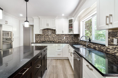 Large trendy l-shaped ceramic tile eat-in kitchen photo in Vancouver with shaker cabinets, white cabinets, an island, an undermount sink, stainless steel appliances, granite countertops, multicolored backsplash and glass tile backsplash