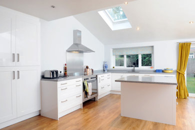 This is an example of a contemporary kitchen in West Midlands with flat-panel cabinets, white cabinets, granite worktops, metallic splashback, medium hardwood flooring and an island.