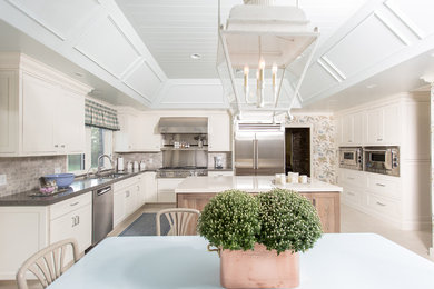 This is an example of a large farmhouse u-shaped kitchen/diner in Other with a submerged sink, shaker cabinets, white cabinets, composite countertops, grey splashback, metro tiled splashback, stainless steel appliances, light hardwood flooring and an island.