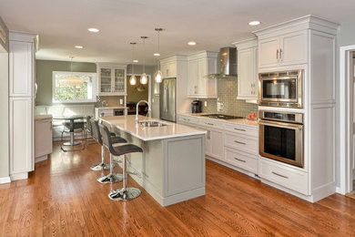 Example of a mid-sized transitional galley medium tone wood floor eat-in kitchen design in New York with an undermount sink, shaker cabinets, white cabinets, quartz countertops, gray backsplash, glass tile backsplash, stainless steel appliances and an island