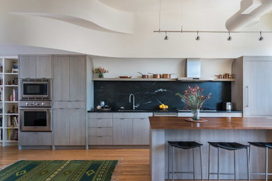 Foto på ett mellanstort funkis kök, med en undermonterad diskho, släta luckor, bänkskiva i täljsten, svart stänkskydd, stänkskydd i sten, integrerade vitvaror, en köksö, grå skåp, mellanmörkt trägolv och brunt golv