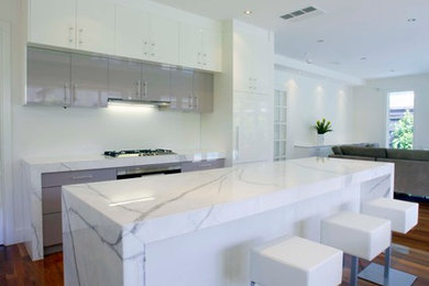 Large trendy l-shaped medium tone wood floor eat-in kitchen photo in Melbourne with an undermount sink, flat-panel cabinets, white cabinets, marble countertops, white backsplash, glass sheet backsplash, stainless steel appliances and an island