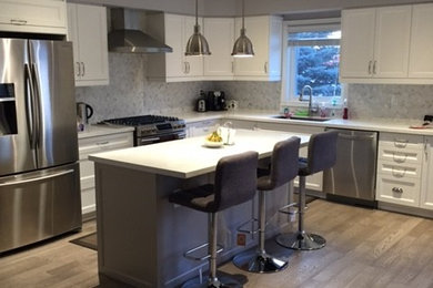 Example of a mid-sized transitional l-shaped light wood floor eat-in kitchen design in Toronto with shaker cabinets, white cabinets, solid surface countertops, gray backsplash, an island, an undermount sink, matchstick tile backsplash and stainless steel appliances