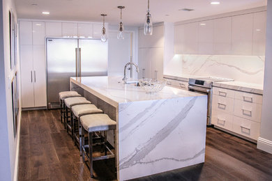Example of a minimalist u-shaped dark wood floor and brown floor enclosed kitchen design in Tampa with an undermount sink, white cabinets, quartz countertops, white backsplash and an island