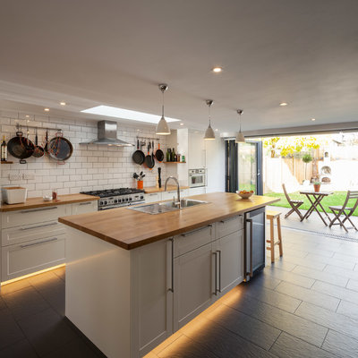 Inspiration for a mid-sized transitional galley ceramic tile kitchen remodel in London with a single-bowl sink, recessed-panel cabinets, white cabinets, wood countertops, white backsplash, stainless steel appliances, an island and subway tile backsplash
