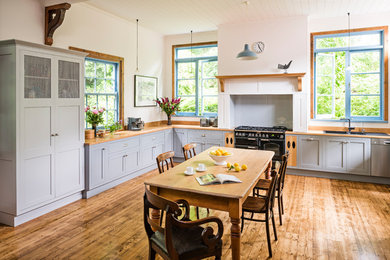Bild på ett stort vintage kök, med en dubbel diskho, grå skåp, träbänkskiva, brunt stänkskydd, stänkskydd i trä, svarta vitvaror, mellanmörkt trägolv, brunt golv och skåp i shakerstil