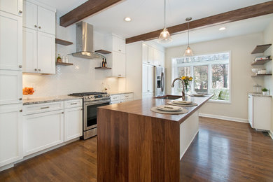 Large transitional galley medium tone wood floor kitchen photo in Cleveland with an undermount sink, shaker cabinets, white cabinets, wood countertops, white backsplash, ceramic backsplash, stainless steel appliances and an island