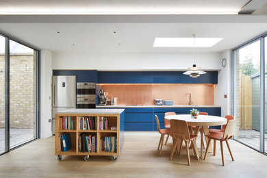 Design ideas for a contemporary single-wall kitchen/diner in London with flat-panel cabinets, blue cabinets, metallic splashback, stainless steel appliances, light hardwood flooring, an island and beige floors.