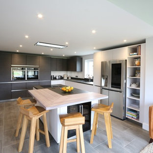 Inspiration for a medium sized contemporary l-shaped open plan kitchen in Buckinghamshire with a submerged sink, flat-panel cabinets, stainless steel appliances, an island, grey floors and black worktops.