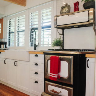 Modelo de cocina en L, de estilo de casa de campo, de tamaño medio, abierta, con fregadero sobremueble, armarios con rebordes decorativos, puertas de armario amarillas, encimera de madera, salpicadero amarillo, electrodomésticos de acero inoxidable, suelo de madera en tonos medios, una isla, suelo marrón y encimeras naranjas