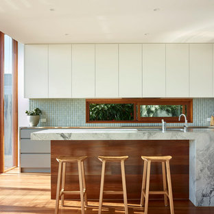 Mid-sized contemporary galley kitchen in Brisbane with an undermount sink, flat-panel cabinets, white cabinets, granite benchtops, green splashback, ceramic splashback, black appliances, medium hardwood floors, with island and brown floor.