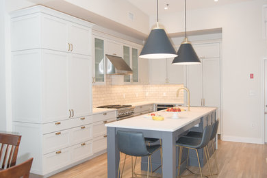 Kitchen - mid-sized modern l-shaped light wood floor and brown floor kitchen idea in New York with an undermount sink, flat-panel cabinets, gray cabinets, quartz countertops, gray backsplash, ceramic backsplash, stainless steel appliances, an island and white countertops
