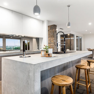 Inspiration for a mid-sized contemporary galley open plan kitchen in Melbourne with light wood cabinets, concrete benchtops, black splashback, limestone floors, with island, grey floor, a single-bowl sink, flat-panel cabinets, grey benchtop and window splashback.