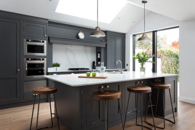 Design ideas for a medium sized classic single-wall open plan kitchen in Dublin with a single-bowl sink, shaker cabinets, grey cabinets, quartz worktops, white splashback, engineered quartz splashback, stainless steel appliances, light hardwood flooring, an island, brown floors, white worktops and a vaulted ceiling.