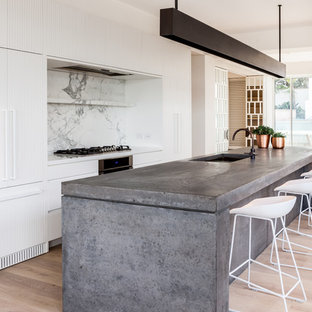 Inspiration for a contemporary galley kitchen in Sydney with an undermount sink, flat-panel cabinets, white cabinets, white splashback, stone slab splashback, panelled appliances, light hardwood floors, with island, beige floor and white benchtop.
