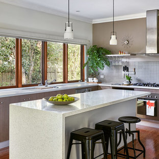 Design ideas for a mid-sized contemporary u-shaped open plan kitchen in Melbourne with flat-panel cabinets, light wood cabinets, solid surface benchtops, grey splashback, with island, white benchtop, an undermount sink, ceramic splashback, stainless steel appliances, medium hardwood floors and brown floor.
