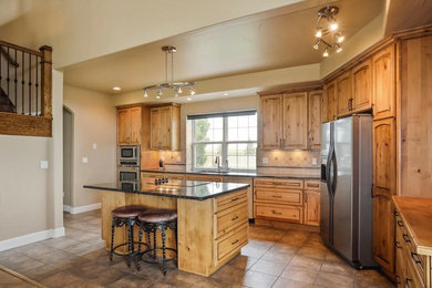 Kitchen - mid-sized traditional l-shaped brown floor kitchen idea in Denver with an undermount sink, raised-panel cabinets, light wood cabinets, stainless steel appliances, an island, granite countertops, beige backsplash and travertine backsplash