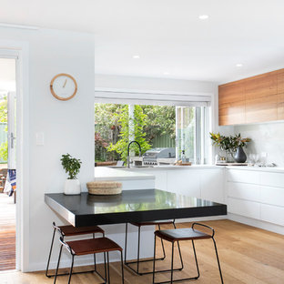 Contemporary u-shaped eat-in kitchen in Wollongong with an undermount sink, flat-panel cabinets, white cabinets, white splashback, stainless steel appliances, medium hardwood floors, brown floor and white benchtop.