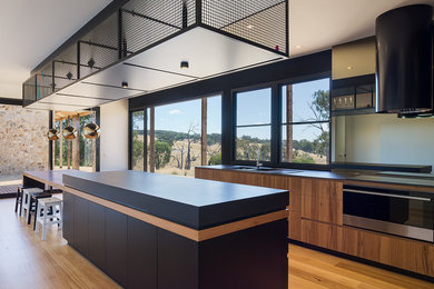 Zweizeilige Moderne Wohnküche mit Kücheninsel, Einbauwaschbecken, flächenbündigen Schrankfronten, schwarzen Schränken, Küchenrückwand in Weiß, Küchengeräten aus Edelstahl, braunem Holzboden, braunem Boden und schwarzer Arbeitsplatte in Melbourne