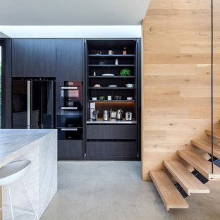 Contemporary l-shaped kitchen in Melbourne with with island, flat-panel cabinets, black cabinets, black appliances, concrete floors, grey floor and white benchtop.