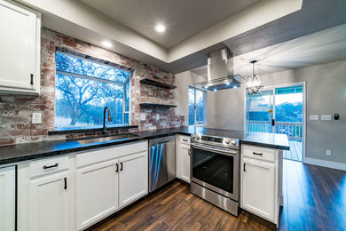 Example of a mid-sized transitional u-shaped dark wood floor and brown floor enclosed kitchen design in Other with a triple-bowl sink, recessed-panel cabinets, white cabinets, granite countertops, red backsplash, brick backsplash, stainless steel appliances and a peninsula