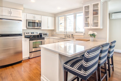 Example of a mid-sized beach style u-shaped medium tone wood floor and brown floor kitchen design in Portland Maine with an undermount sink, shaker cabinets, white cabinets, quartzite countertops, stainless steel appliances, a peninsula and white countertops