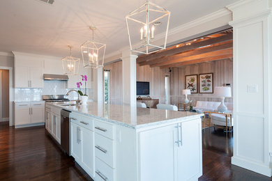 This is an example of a large bohemian u-shaped enclosed kitchen in New York with a submerged sink, shaker cabinets, white cabinets, engineered stone countertops, white splashback, metro tiled splashback, stainless steel appliances, medium hardwood flooring, an island and brown floors.