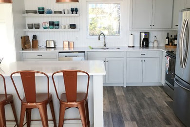 Exempel på ett litet maritimt kök, med en undermonterad diskho, skåp i shakerstil, blå skåp, bänkskiva i kvarts, vitt stänkskydd, stänkskydd i trä, rostfria vitvaror, laminatgolv, en köksö och grått golv