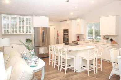 Example of a mid-sized beach style l-shaped medium tone wood floor and brown floor eat-in kitchen design in Tampa with an undermount sink, white cabinets, stainless steel appliances, an island, gray backsplash and matchstick tile backsplash