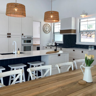 Mid-sized beach style l-shaped eat-in kitchen in Gold Coast - Tweed with an undermount sink, shaker cabinets, white cabinets, blue splashback, stainless steel appliances, with island and white benchtop.