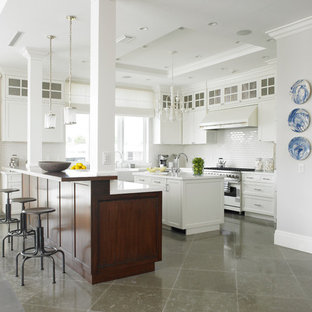 Ejemplo de cocina en L, clásica renovada, grande, con fregadero sobremueble, armarios estilo shaker, puertas de armario blancas, electrodomésticos de acero inoxidable, suelo de piedra caliza, una isla, salpicadero blanco y salpicadero de azulejos tipo metro