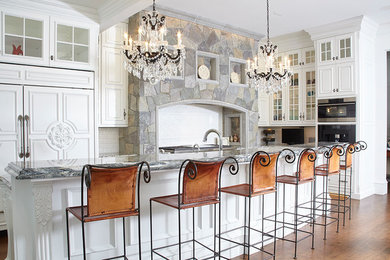 Eat-in kitchen - huge traditional l-shaped dark wood floor and brown floor eat-in kitchen idea in Boston with an undermount sink, raised-panel cabinets, white cabinets, granite countertops, white backsplash, porcelain backsplash, paneled appliances and an island