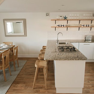 Design ideas for a small coastal u-shaped kitchen/diner in Other with flat-panel cabinets, white cabinets, granite worktops, a breakfast bar, brown floors and grey worktops.