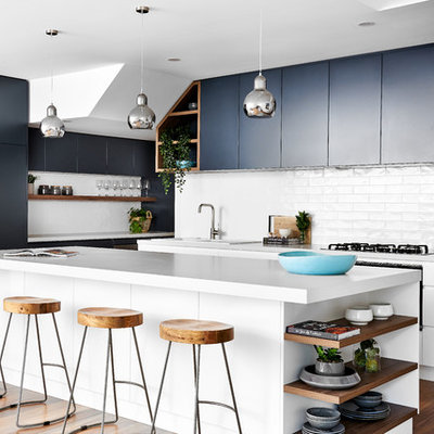 Inspiration for a mid-sized coastal medium tone wood floor kitchen remodel in Sydney with a double-bowl sink, flat-panel cabinets, quartz countertops, white backsplash, an island, white countertops, subway tile backsplash, black cabinets and black appliances