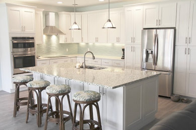 Inspiration for a mid-sized coastal l-shaped medium tone wood floor and brown floor kitchen remodel in Miami with an undermount sink, shaker cabinets, white cabinets, terrazzo countertops, green backsplash, matchstick tile backsplash, stainless steel appliances and an island