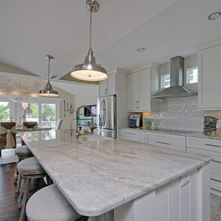 Mid-sized beach style single-wall open plan kitchen in Tampa with a farmhouse sink, shaker cabinets, white cabinets, granite benchtops, white splashback, ceramic splashback, stainless steel appliances, vinyl floors and with island.