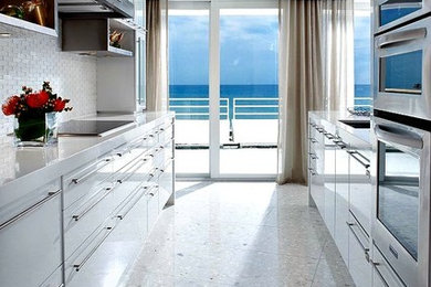 Trendy galley beige floor kitchen photo in Miami with an undermount sink, flat-panel cabinets, white cabinets, white backsplash, stainless steel appliances and white countertops
