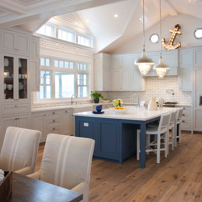 Beach style l-shaped medium tone wood floor and brown floor eat-in kitchen photo in San Diego with a farmhouse sink, recessed-panel cabinets, white cabinets, white backsplash, subway tile backsplash, paneled appliances and an island