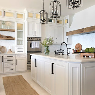Photo of a nautical u-shaped kitchen in San Diego with raised-panel cabinets, white cabinets, white splashback, stainless steel appliances, an island, beige floors and beige worktops.