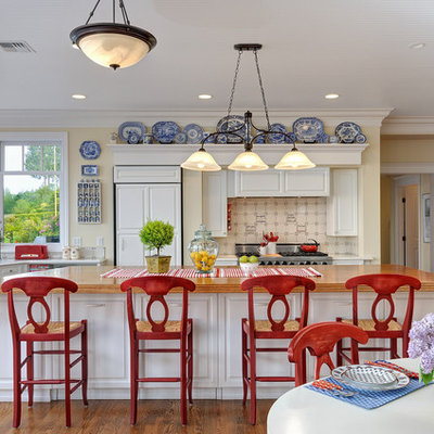 Example of a large beach style l-shaped medium tone wood floor eat-in kitchen design in Seattle with wood countertops, paneled appliances, raised-panel cabinets, an island, white cabinets, beige backsplash and ceramic backsplash